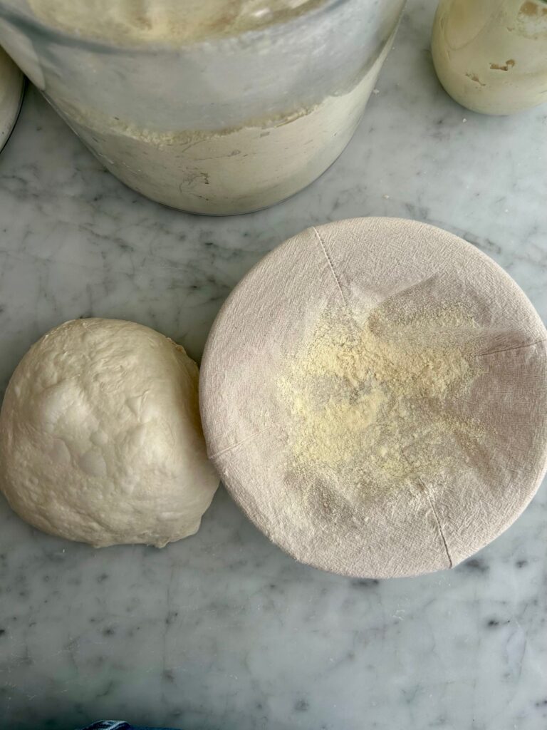 sourdough ball next to a floured banneton basket