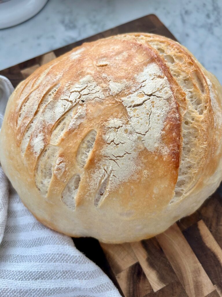 Whole loaf of baked sourdough bread on wood cutting board