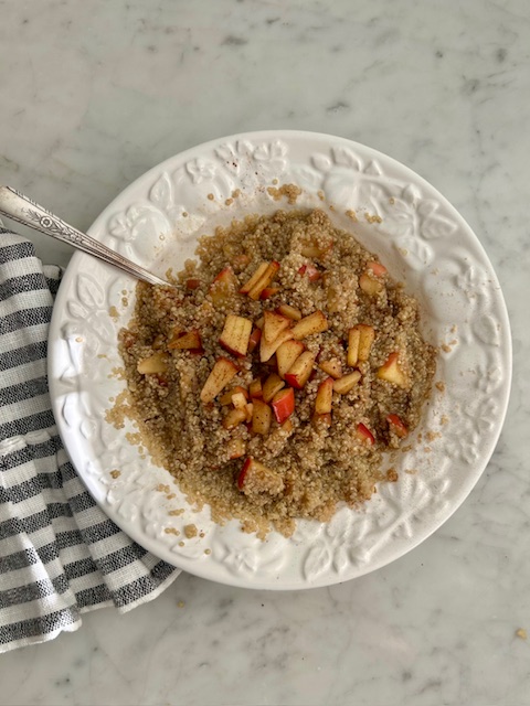 apple cinnamon quinoa in white serving bowl with silver serving spoon on white countertop