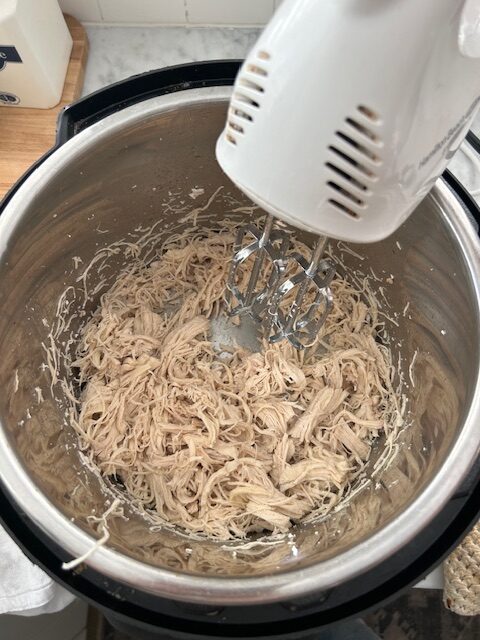shredded chicken in instant pot being shredded with a hand mixer
