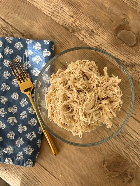 cooked shredded chicken in glass bowl ready to eat with a napkin and fork